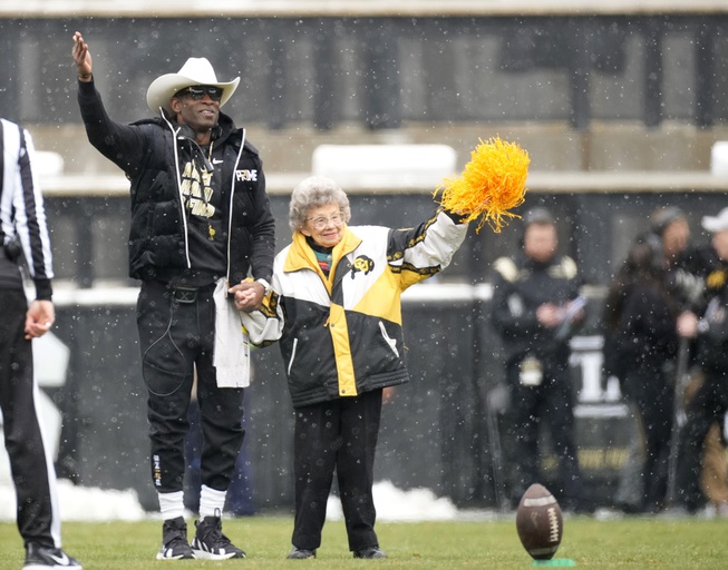 Colorado coach Deion Sanders, left, leads longtime supporter Peggy Coppom to kick the football before the team's spring practice NCAA college football game April 22, 2023, in Boulder, Colo. Coppom, 98, said she's excited about Colorado's return to the Big 12 in 2024. She has attended Colorado football games since 1940.