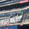 From left to right, Nina Thorsen, of Alameda, Calif., along with an As usher and Will MacNeil, of Dublin, Calif., tape homemade signs to the right-field fence at the Oakland-Alameda Coliseum on Saturday, Aug. 19, 2023. Thorsen and MacNeil are part of the Oakland 68s, a group of A's megafans partnering with the Nevada State Education Association to circulate a petition to repeal a public financing bill for a new A's stadium in Las Vegas.