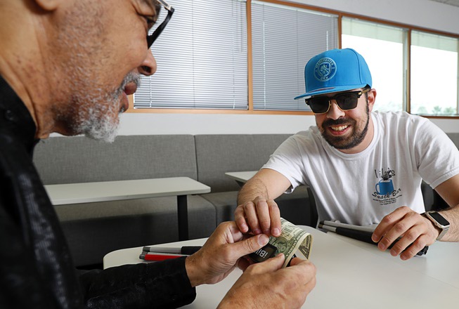 Samuel Hall, left, gets help from Ivan Delgado as he learns to use an iBill reader at a Nevada Department of Employment, Training and Rehabilitation (DETR) office on West Charleston Boulevard Friday, March 22, 2024. The device reads aloud the denomination of a bill so that blind people can identify them.
