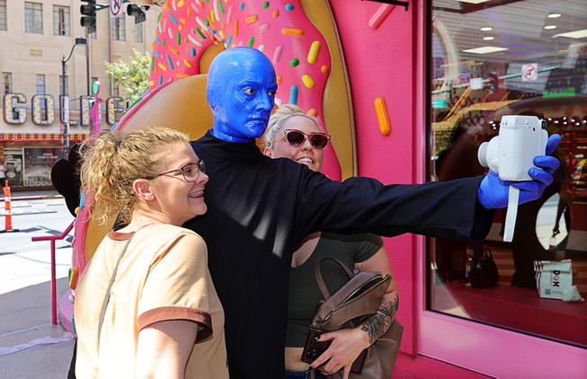 A member of Blue Man Group takes a selfie with guests during a promotional kick-off for Blue Man Group-inspired doughnuts at The Plaza in downtown Las Vegas Friday, April 12, 2024. The limited-edition doughnuts are called Blue Poo and Throwdown.