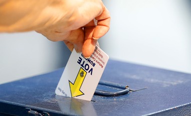 A voter deposits a voting machine activation card into a box during the first day of early voting at the Galleria at Sunset mall Saturday, Oct. 19, 2024, in Henderson. Voters were reporting wait times of over two&nbsp;hours.