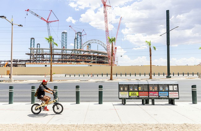 An e-bike rider heads southbound on Las Vegas Boulevard South as construction continues on the Athletics’ stadium in the background Friday, July 24, 2026. The $2 billion stadium is expected to be completed by February 2028.