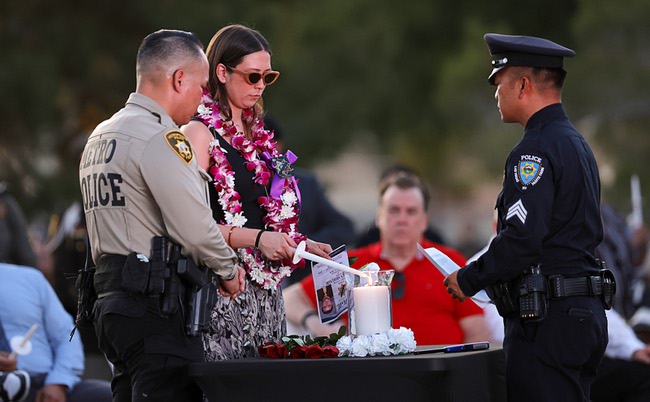 Sage Abdelnabi, center, lights a candle for her husband Metro Police officer Austin Abdelnabi during a vigil at Police Memorial Park Friday, Aug. 7, 2026. Officer Abdelnabi was shot and killed in the line of duty on Tuesday, Aug. 4. With Sage Abdelnabi are Metro Police Lt. Charles Jivapong, left, vice president of the Injured Police Officers Fund, and Sgt. Adrian Calimquim of the Las Vegas Paiute Tribal Police Department.